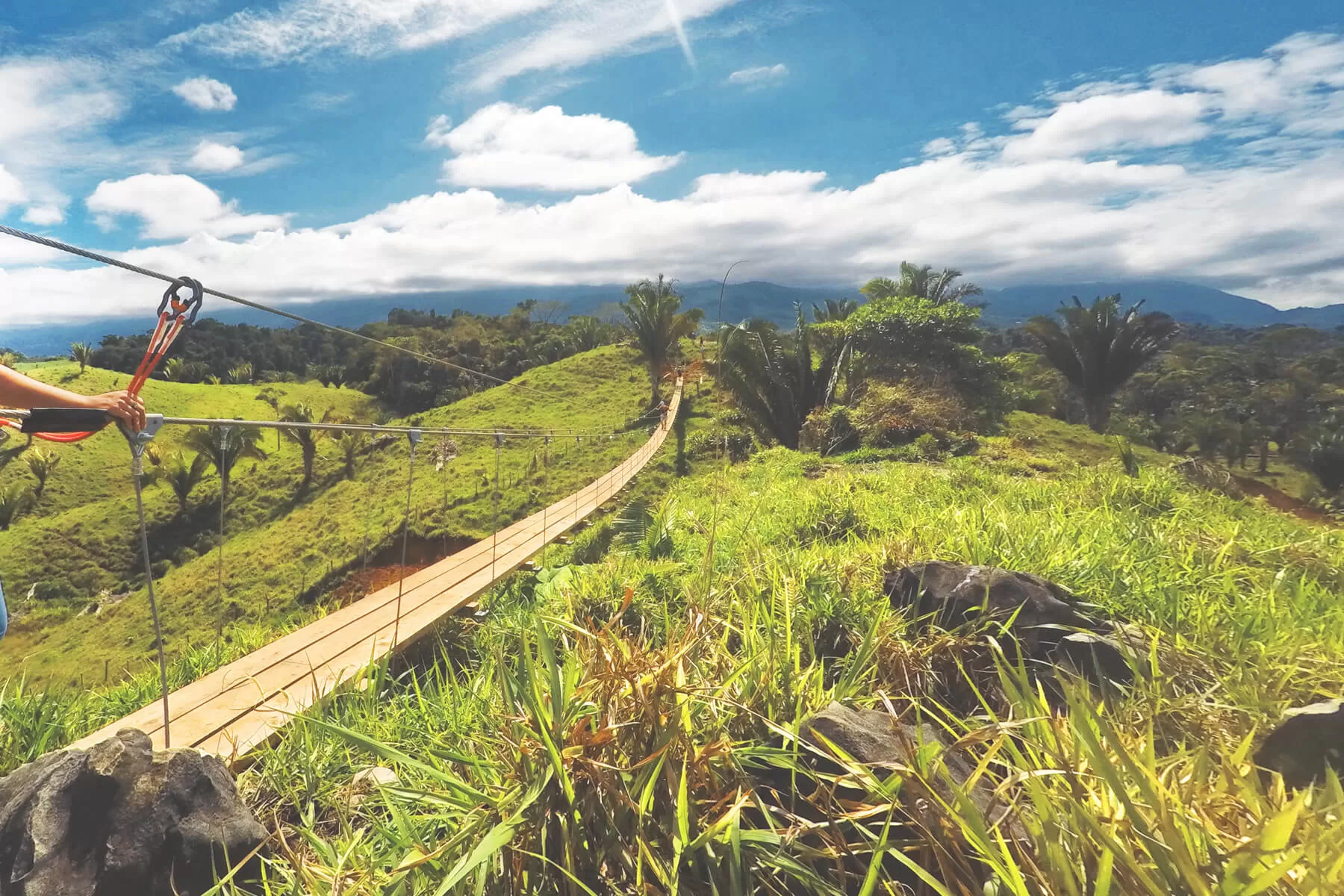 Ecoproparks. Vista de un puente de madera que cruza una montaña llena de césped.