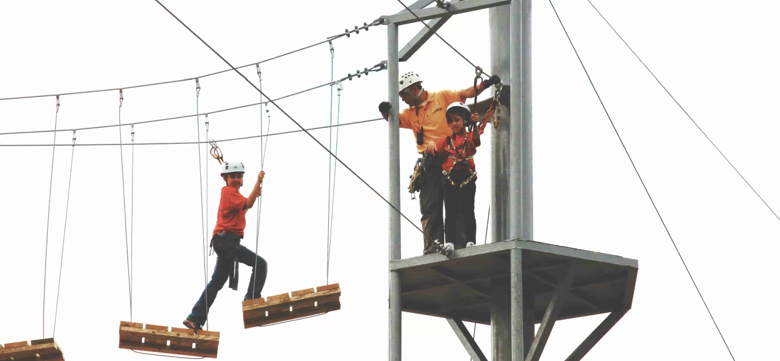 Ecoproparks. Un adulto y dos niños con equipo de protección disfrutando de una emocionante exploración en una torre elevada creada por Ecoproparks.