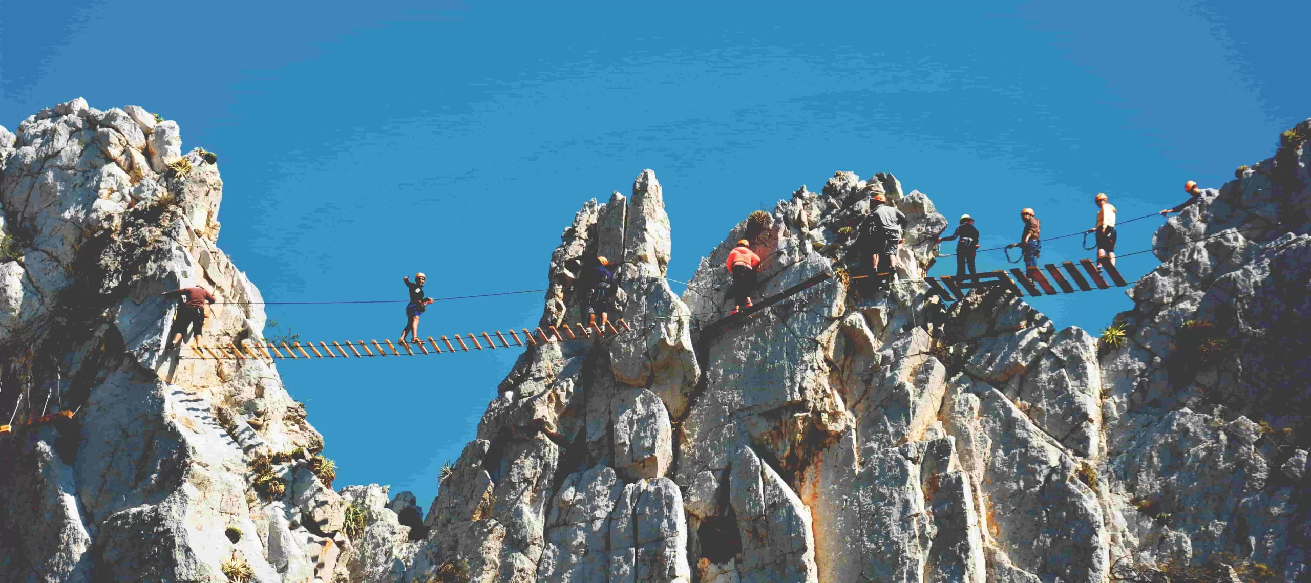 Ecoproparks. Vista amplia de varias personas con protección explorando un hermoso puente de madera que cruza por montañas rocosas, disfrutando de las impresionantes vistas panorámicas.