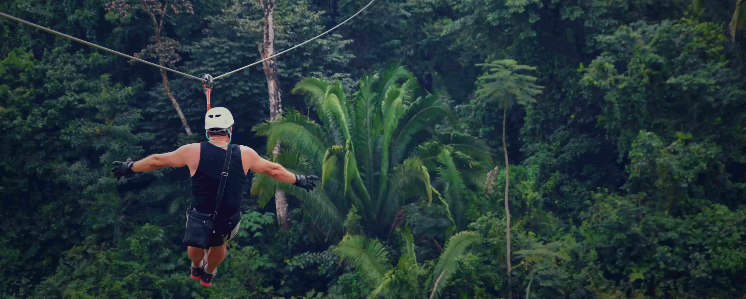 Ecoproparks. Una persona equipada con protección disfrutando de una emocionante tirolesa con una hermosa vista panorámica de una selva exuberante en Ecoproparks.